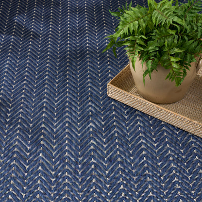 Navy blue chevron rug with speckled texture; beige pot with fern on woven wicker tray.