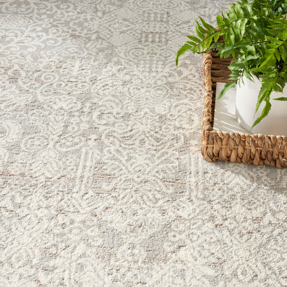 Cream and light gray patterned rug with a subtle damask motif, beside a woven wicker basket with a white pot and green fern.