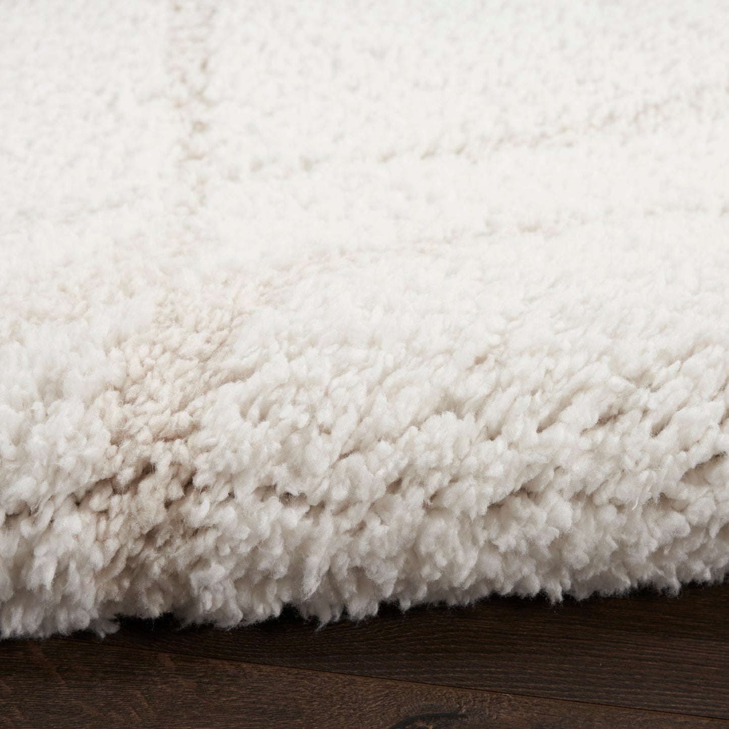 Cream shag rug with dense plush pile resting on dark wooden floor.
