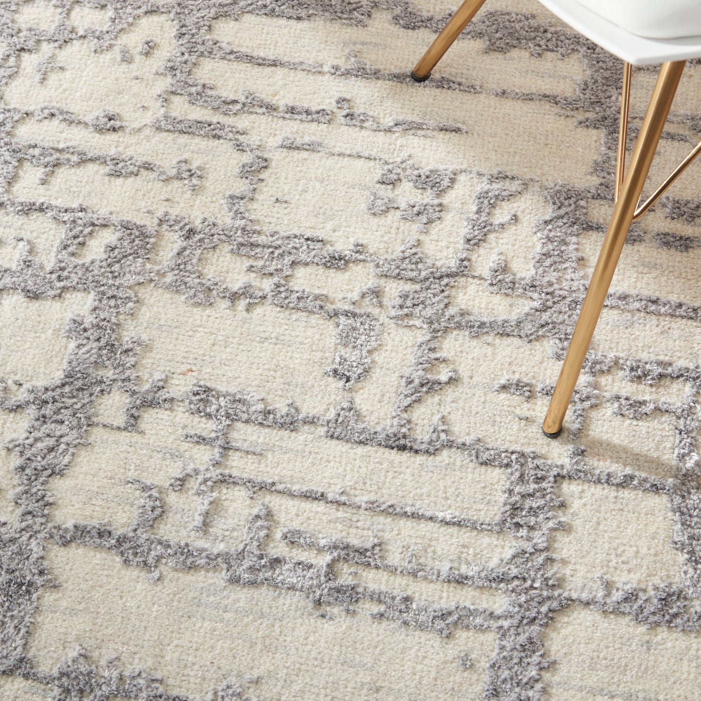 Cream and gray geometric shag rug with a soft fluffy pile; wooden chair legs rest on its patterned surface.