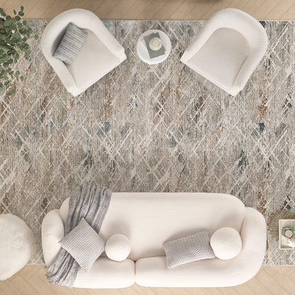 Top-down view of a patterned gray rug in a living room, with a cream sofa, gray knit pillows and blanket, two curved white chairs, and a round side table.