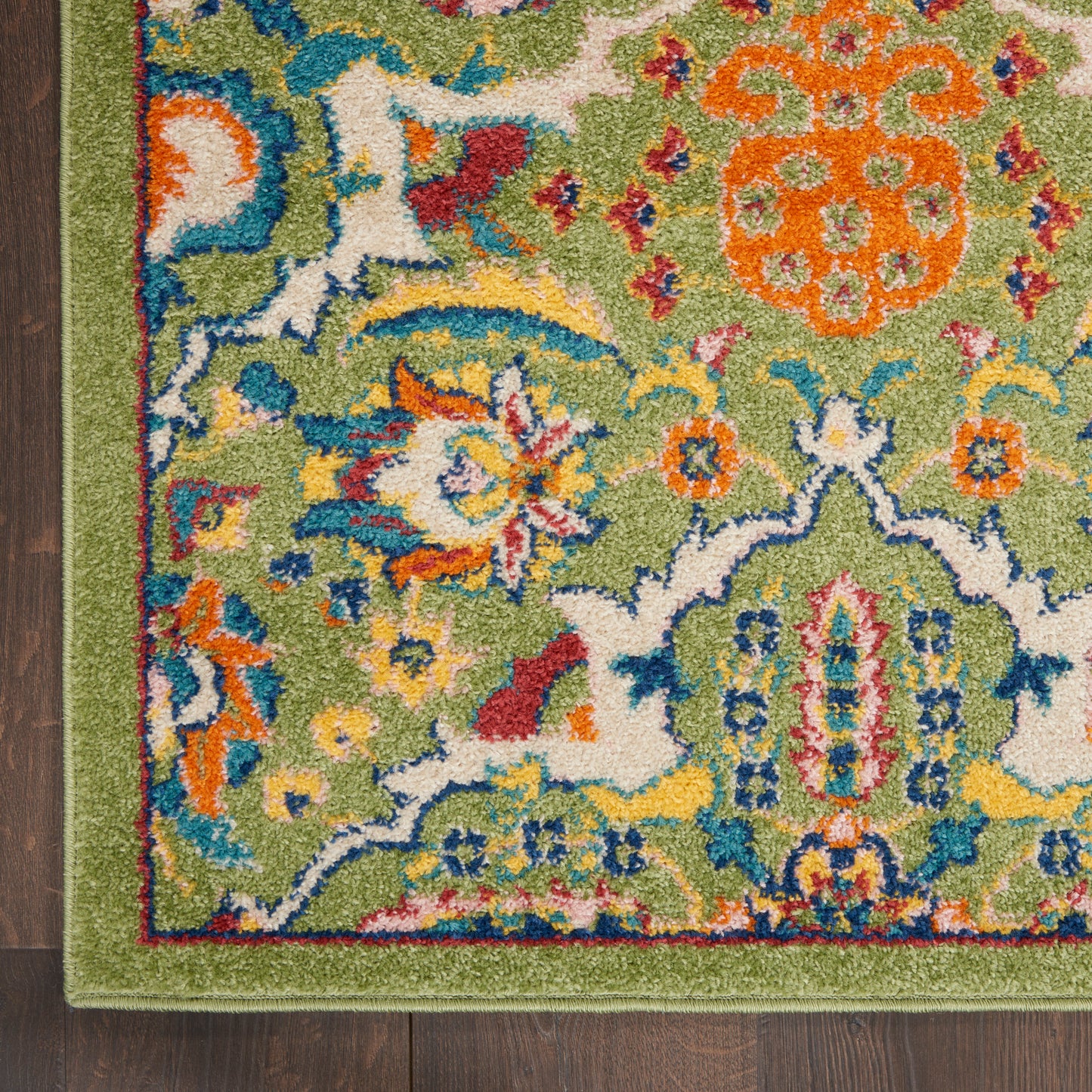 Close-up of a green floral 6' runner rug with blue, orange, white motifs; lime-green border and dark wood floor edge.