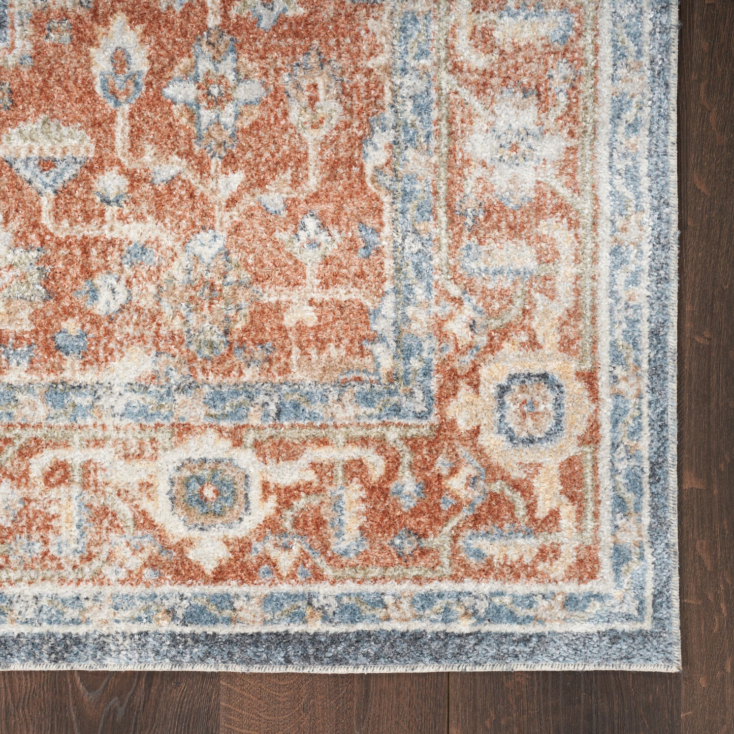 Rust-orange Persian-style rug with blue and cream border and floral motifs on dark wood floor.
