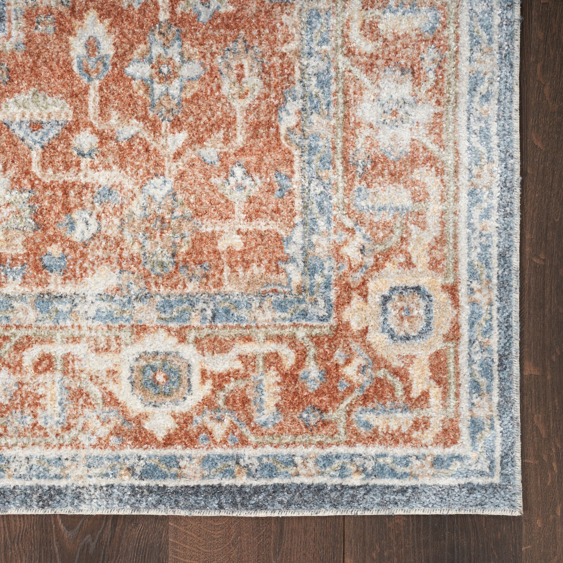 Rust-orange Persian-style rug with blue and cream border and floral motifs on dark wood floor.