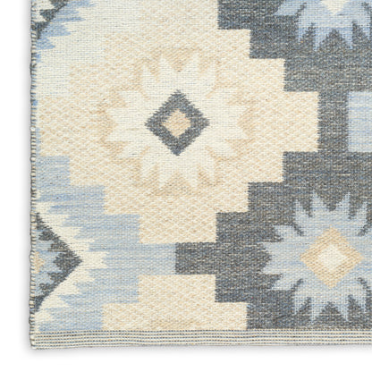 Woven geometric rug with cream sunburst center, pale blue and beige diamonds, dark navy zigzag border and left fringe.