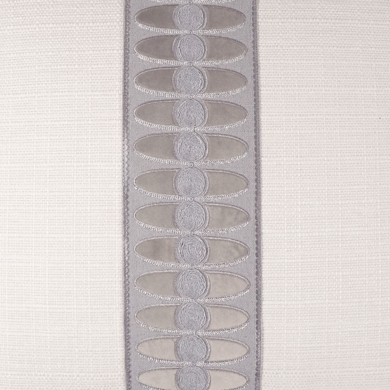 Lavender satin trim with repeated oval embroidered motifs on beige fabric.
