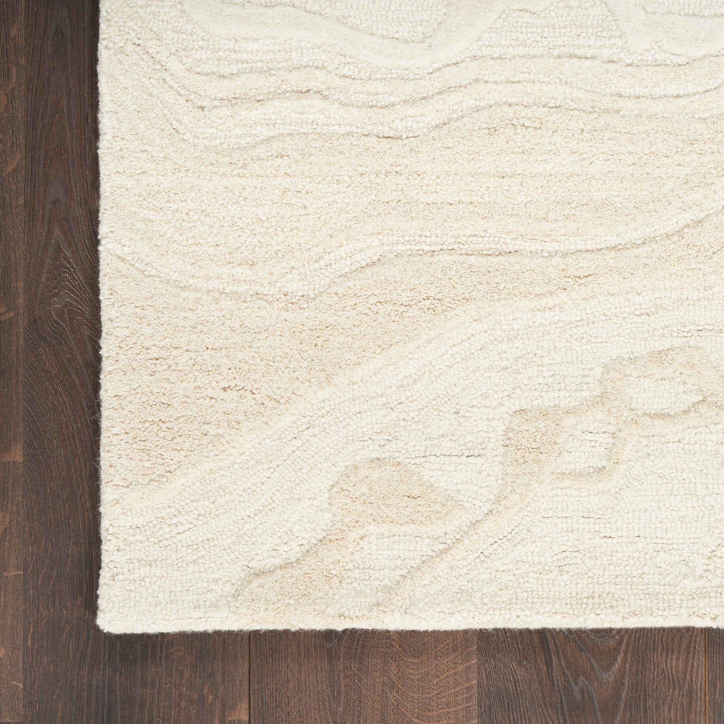 Cream textured area rug with a subtle wave pattern on dark hardwood floor; plush tufted style.
