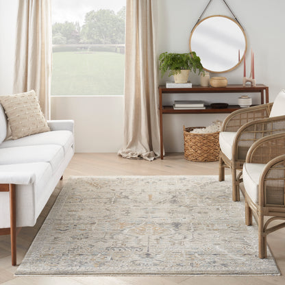 Bright living room with light gray sofa, rattan chairs, blue-gray rug, wooden console, round mirror, plant, beige curtains.