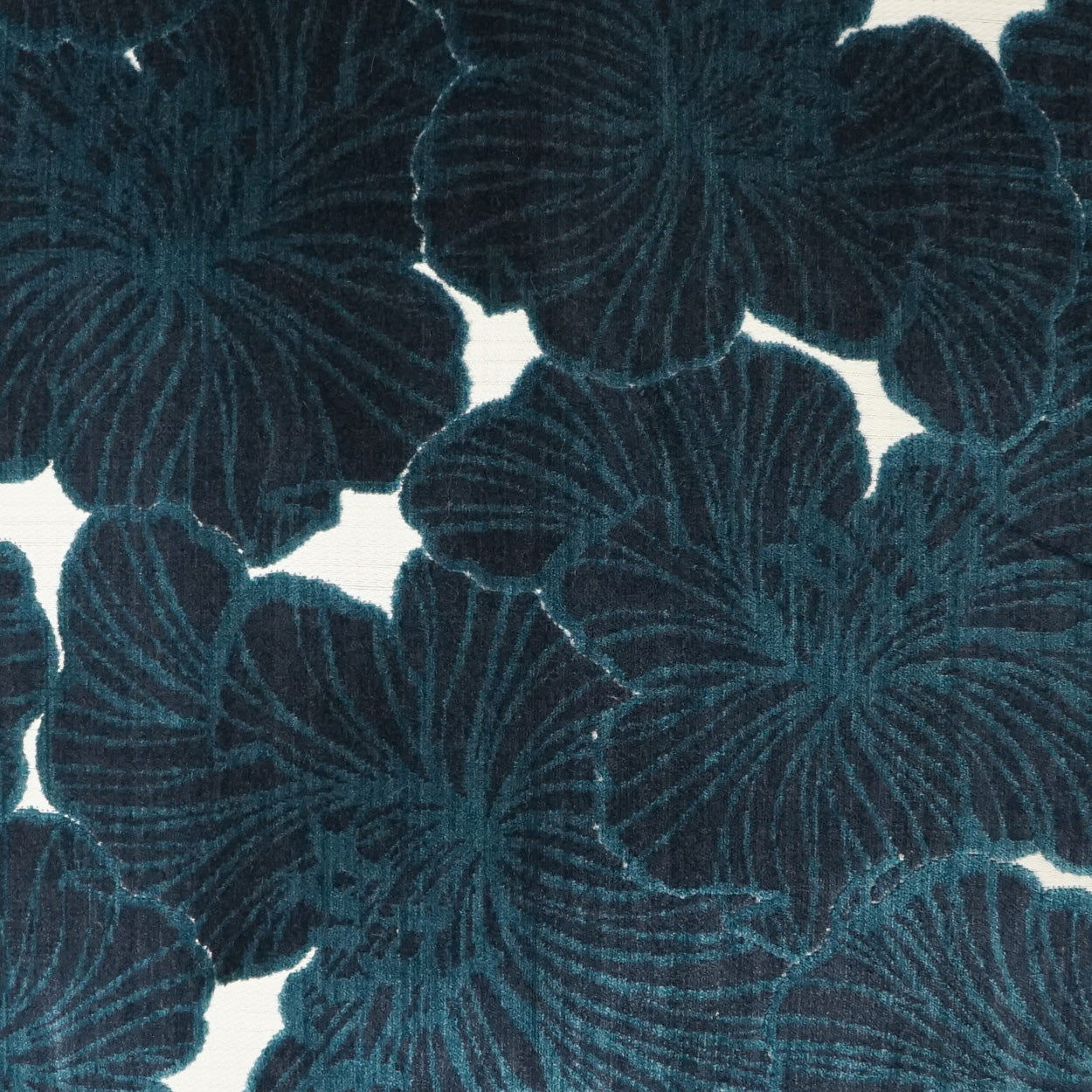 Pillow covered in teal-blue fabric with oversized radiating sapphire floral motifs, 24" x 24".