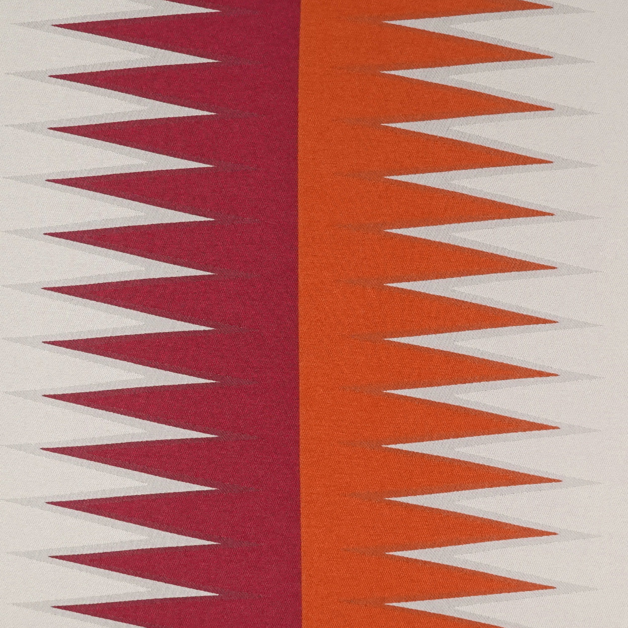 Geometric zigzag fabric with burgundy and orange vertical panels and white triangles on beige background.