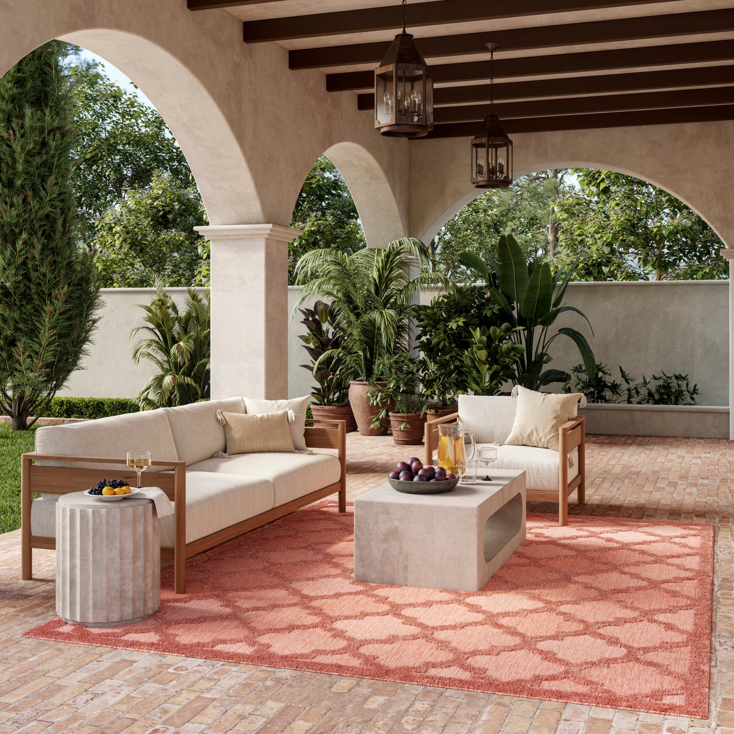 Outdoor patio with archways, brick floor, cushioned sofas, concrete coffee table, coral rug, lanterns, and potted plants.