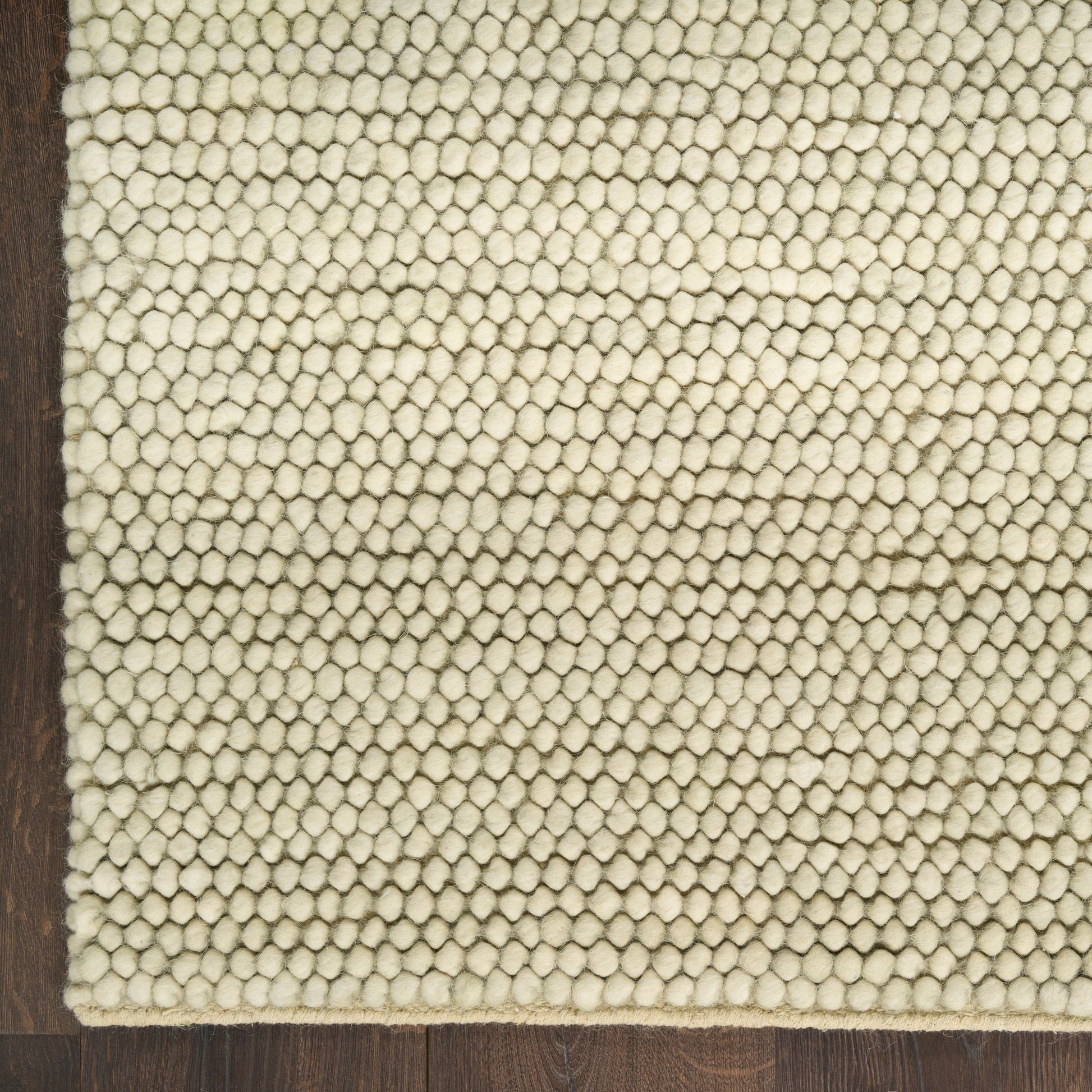 Cream looped-pile rug with dense tiny knots on a dark wooden floor.