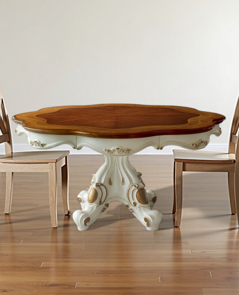Oval dining table with ornate cream pedestal base and dark walnut top; two simple light-wood chairs.