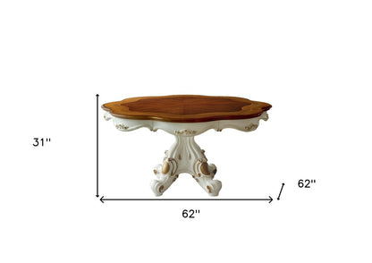 Oval wooden dining table with a warm brown top & ornate white carved pedestal base, 62" long & 31" high.