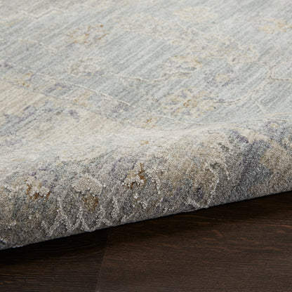 Soft blue-gray low-pile area rug with beige accents and a subtle damask pattern, rolled edge on dark wood floor.