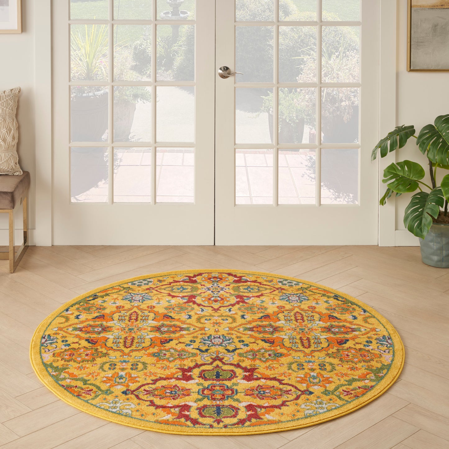 Round oriental rug in warm yellow with multicolor floral pattern on light wood floor by glass French doors.