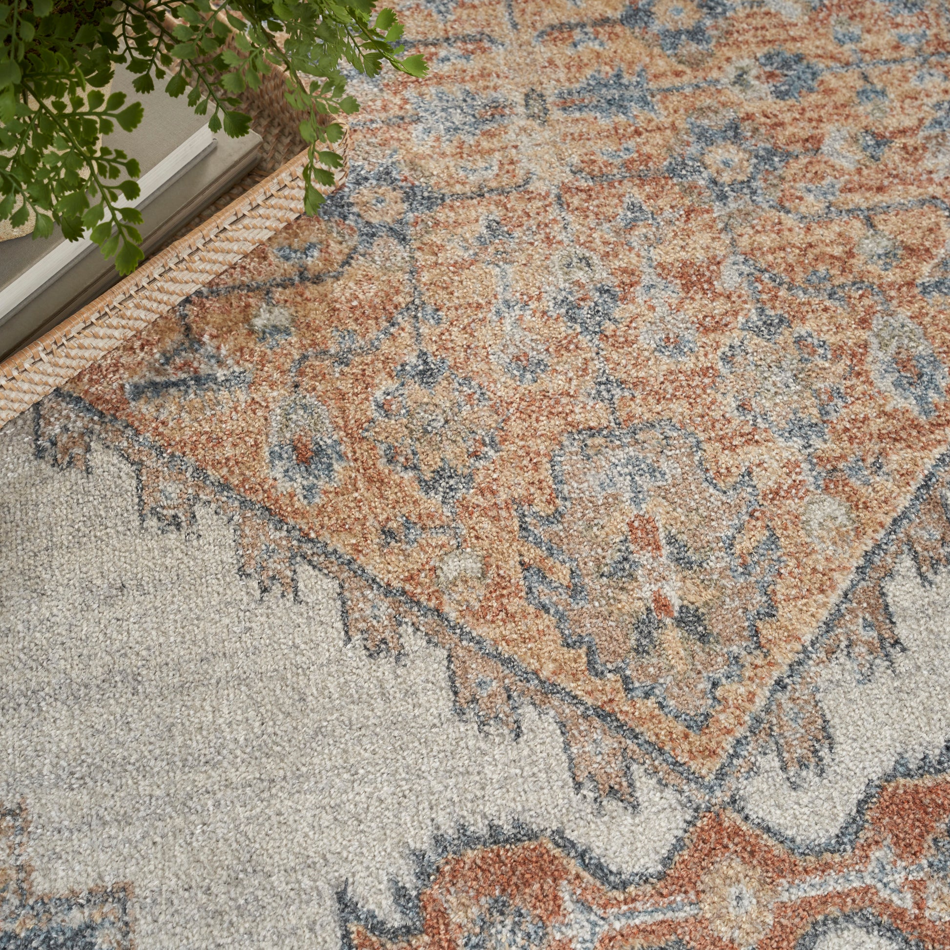 Orange, blue, and beige oriental rug with floral medallions and borders beside a potted green plant.
