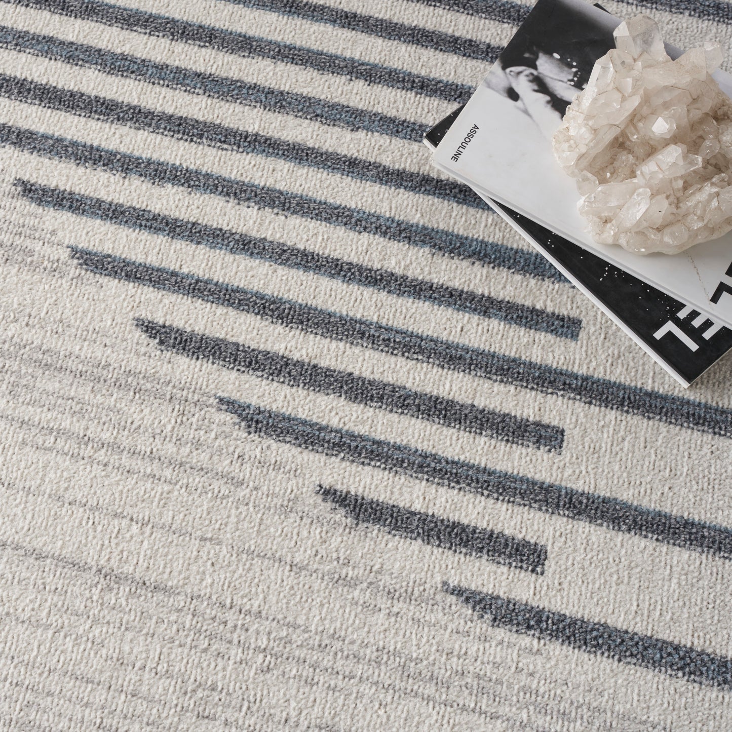Cream textured rug with navy-blue linear stripes; decor items including magazines and a crystal cluster.