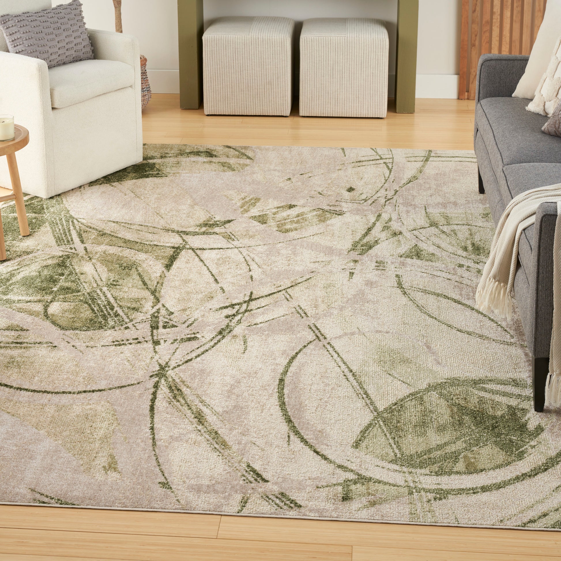 Living room featuring a beige-green abstract botanical rug, white armchair, gray sofa, beige ottomans, and wooden floor.
