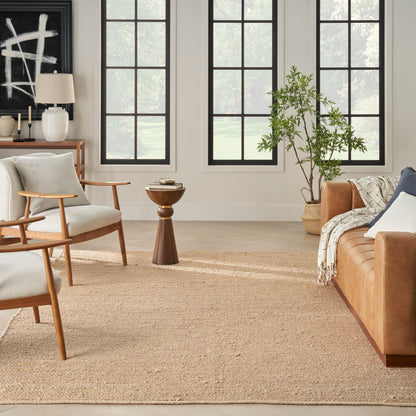 Bright living room with mid-century wood chairs, tan leather sofa, woven rug, large black-framed windows, potted plant.