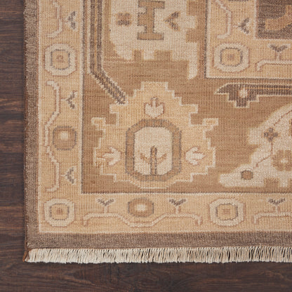 Beige and tan oriental area rug with geometric medallions and fringe edge on dark wood floor.