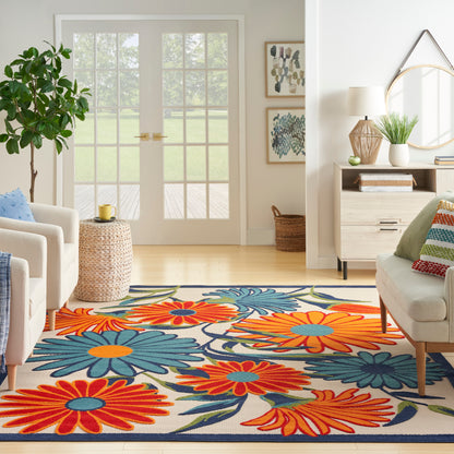 Bright living room with a bold floral rug in orange, teal, blue and cream; light wood furniture and glass French doors.