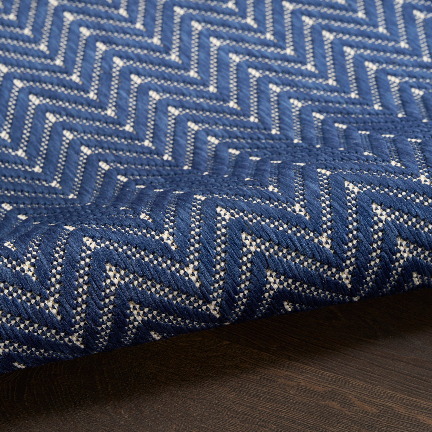 Blue chevron-patterned woven rug with white accents on dark wood floor.