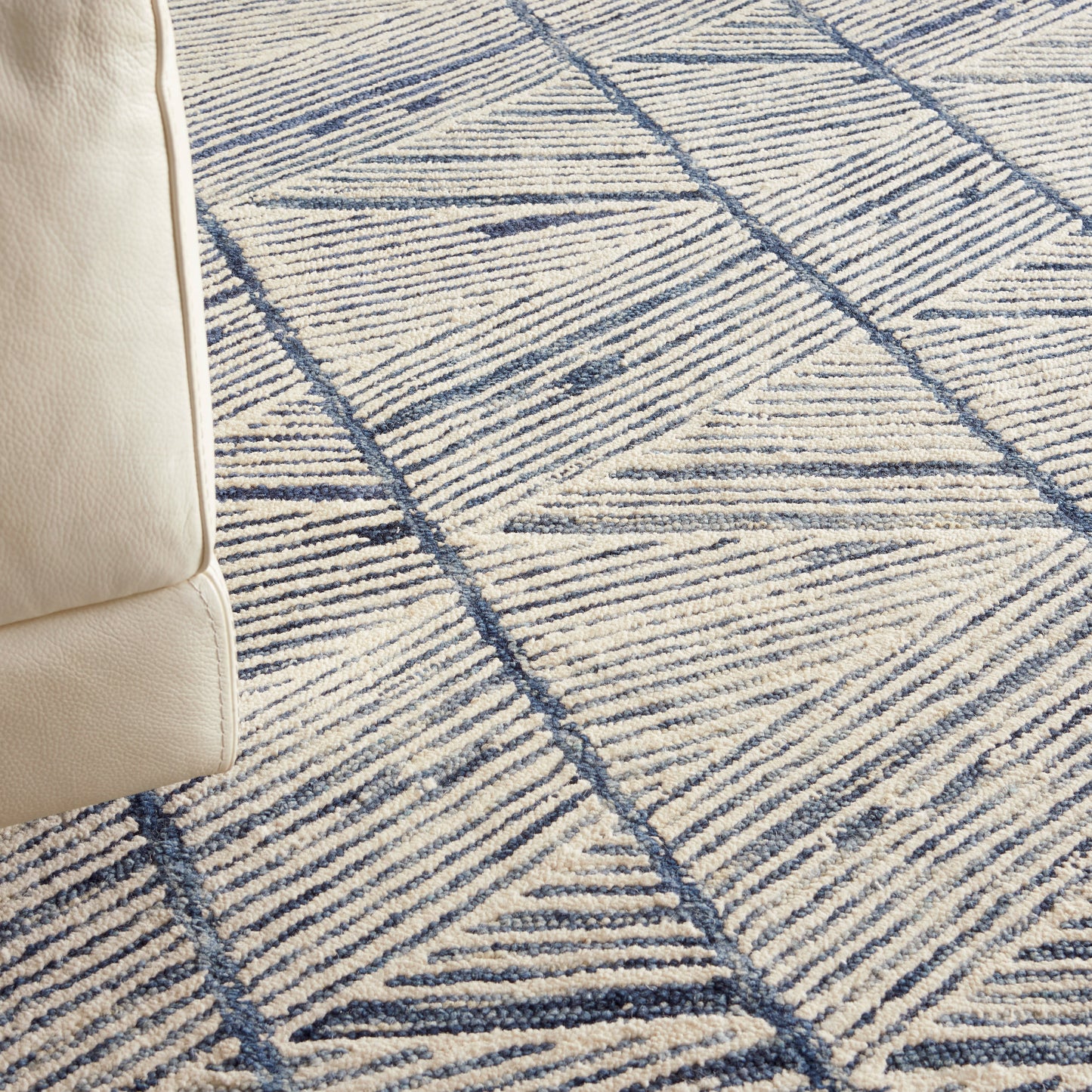Beige leather sofa edge beside a blue geometric rug with triangular line patterns.