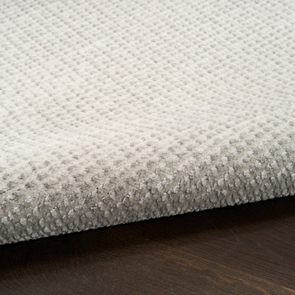 Beige textured rug with tiny raised dot pattern, edge visible on dark wood floor.