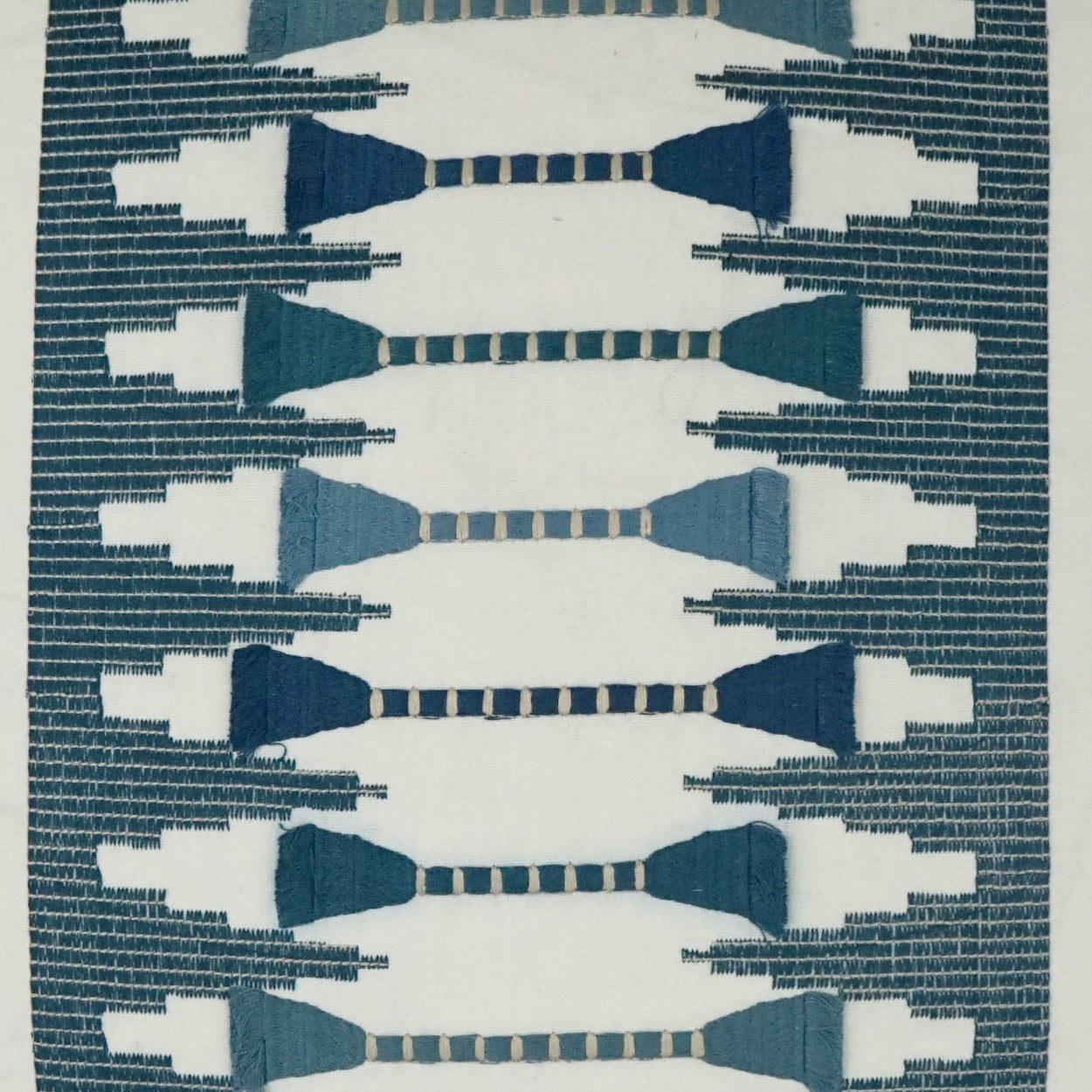 Geometric embroidery on a cream pillow with navy & teal bow-tie motifs and a dark teal border.