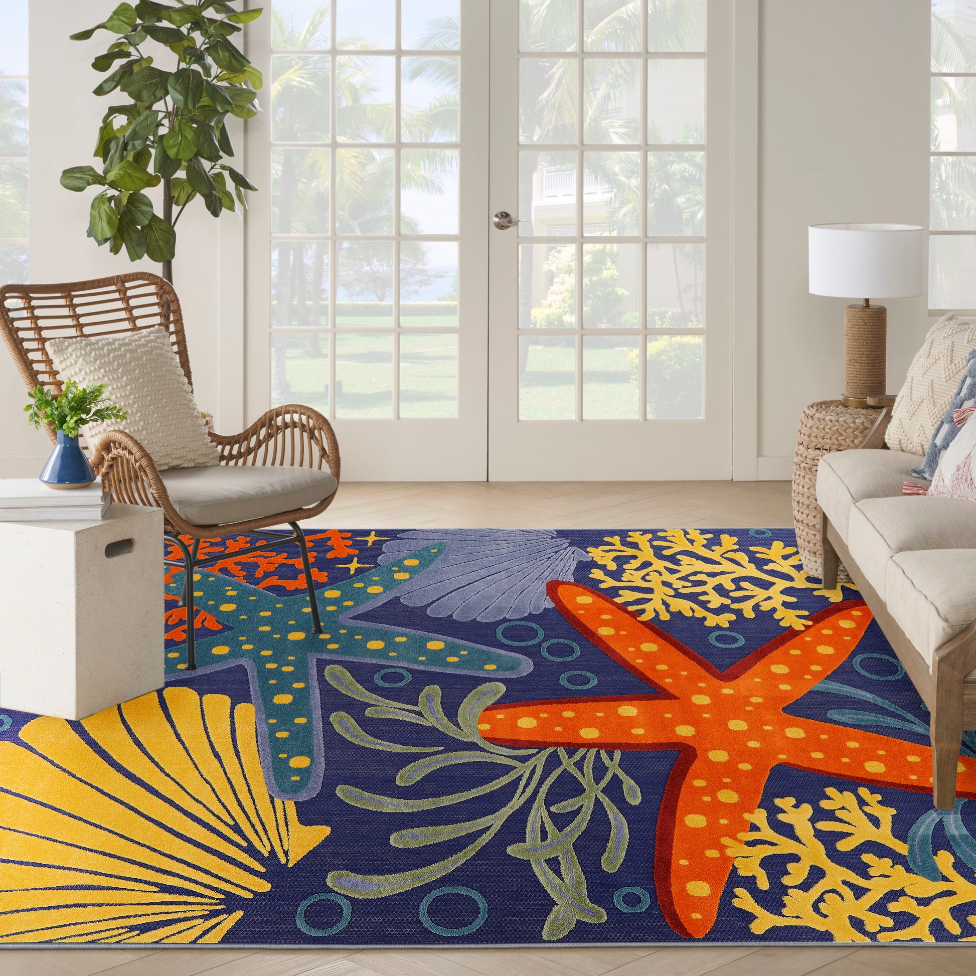 Coastal blue outdoor rug with orange starfish and yellow coral on a sunlit patio with wicker chairs.