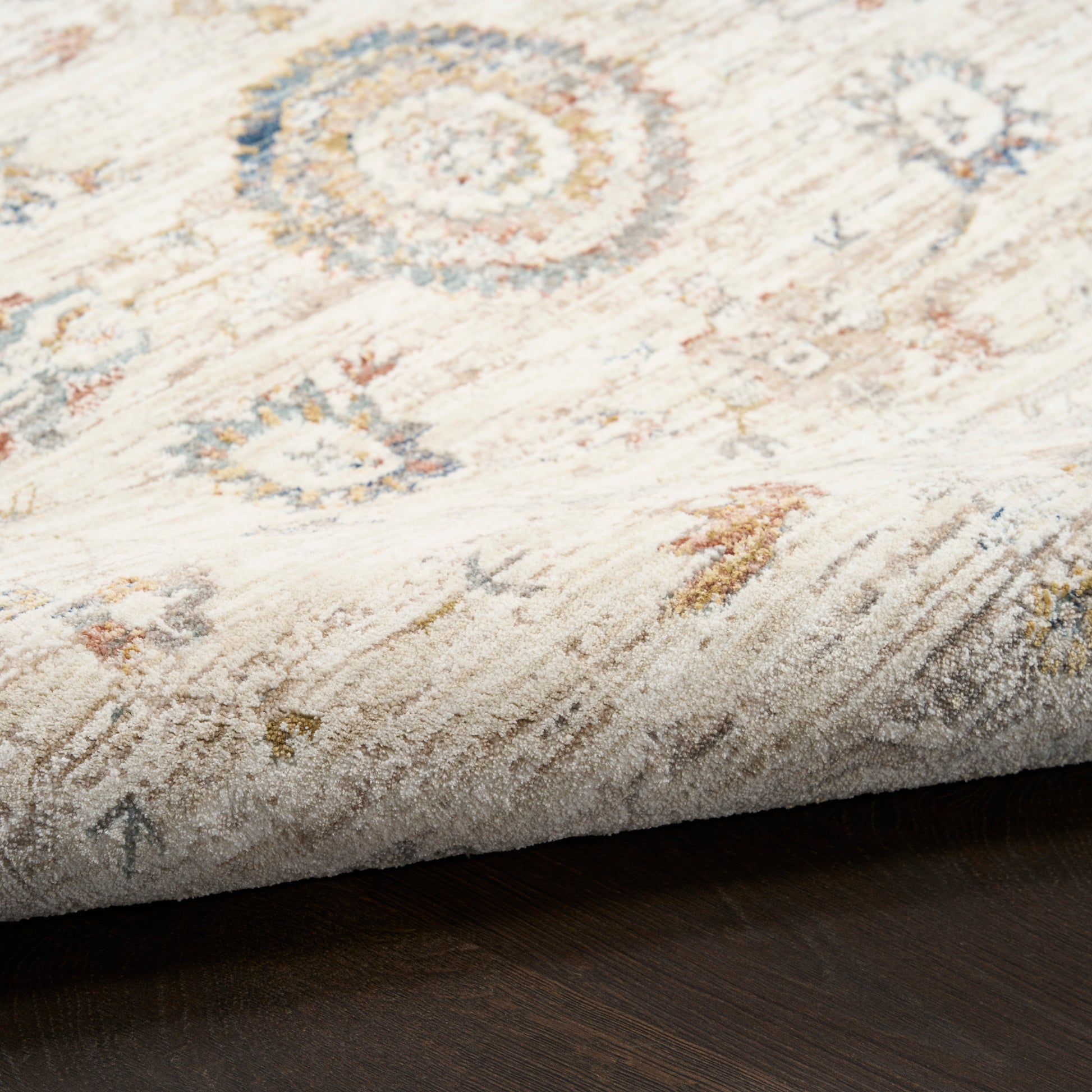 Cream distressed area rug with blue, amber and gray circular medallions on a dark wood floor.
