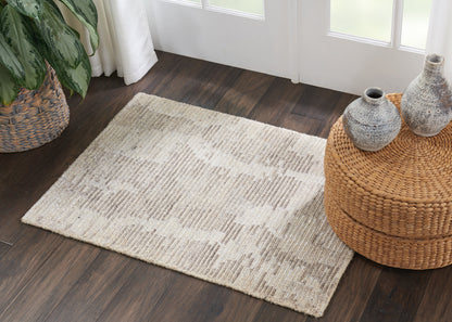 Cream textured area rug with a subtle pattern on dark wood floor, beside a woven round rattan ottoman and ceramic vases.