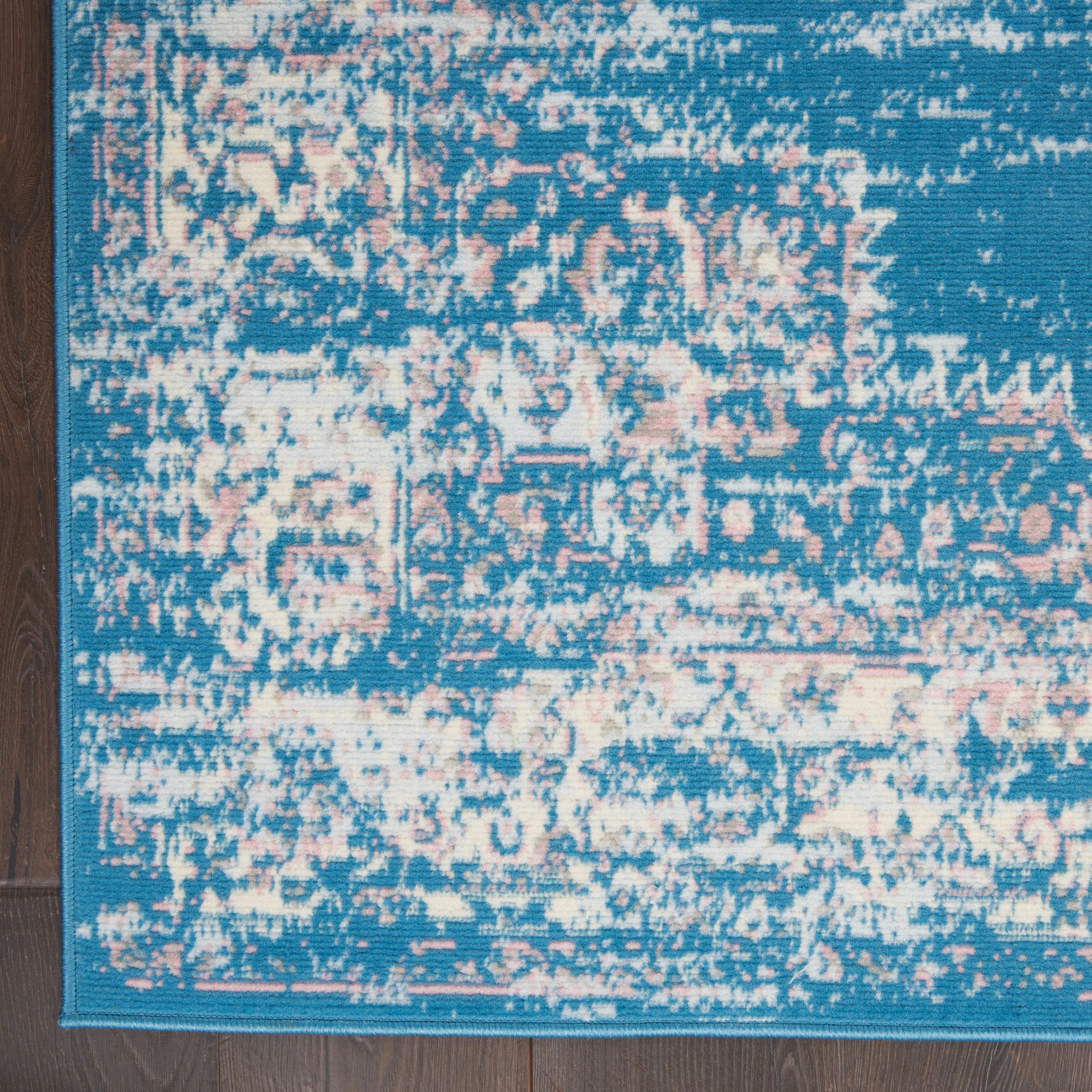 Rectangular turquoise distressed oriental rug with pink-beige motifs on dark wood floor.