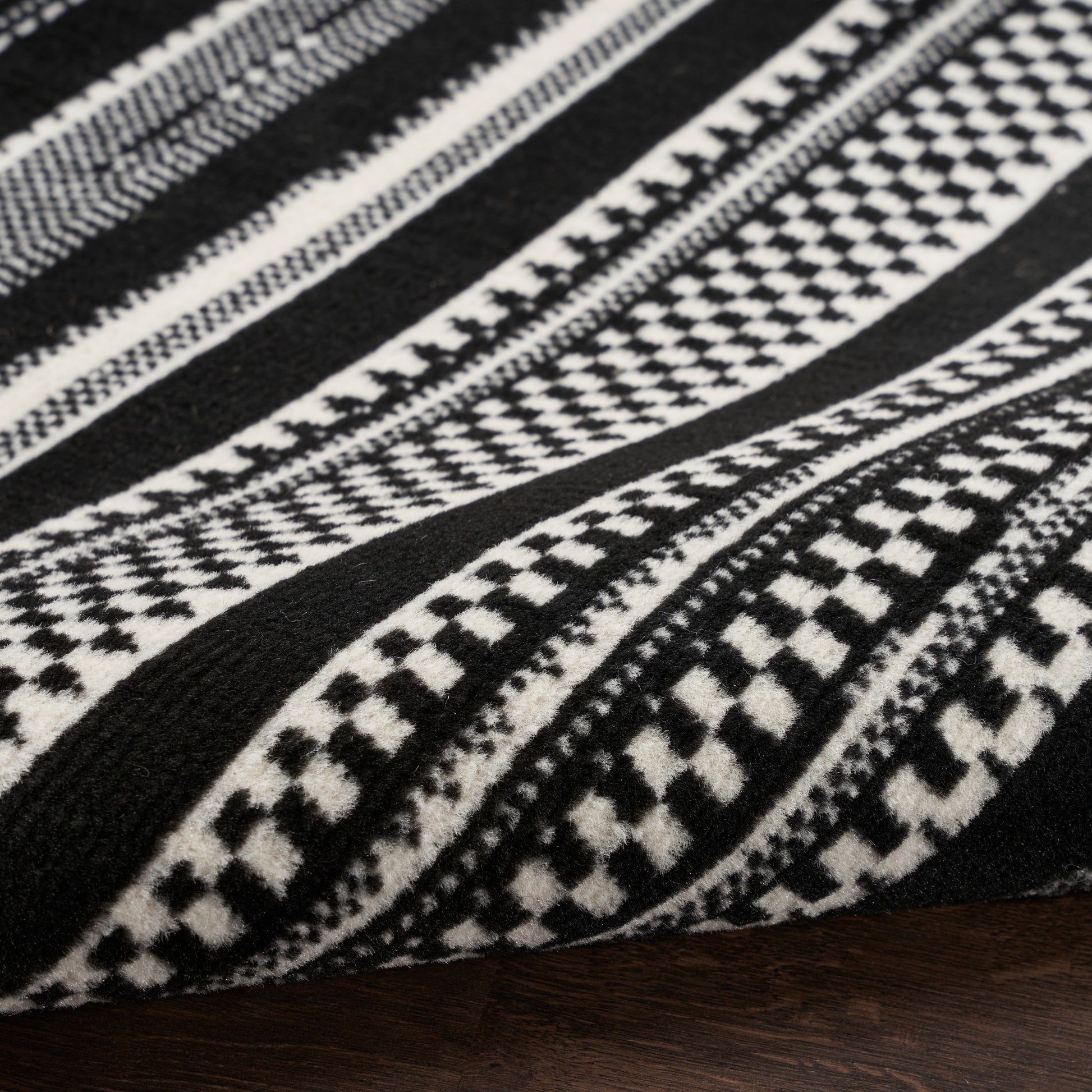 Close-up of black-and-white geometric woven rug with diamond and stripe patterns, thick textile.