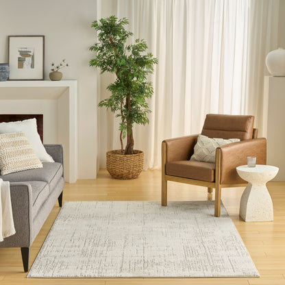Neutral living room with gray fabric sofa, brown leather armchair, light rug, tall plant in woven basket, and white curtains.