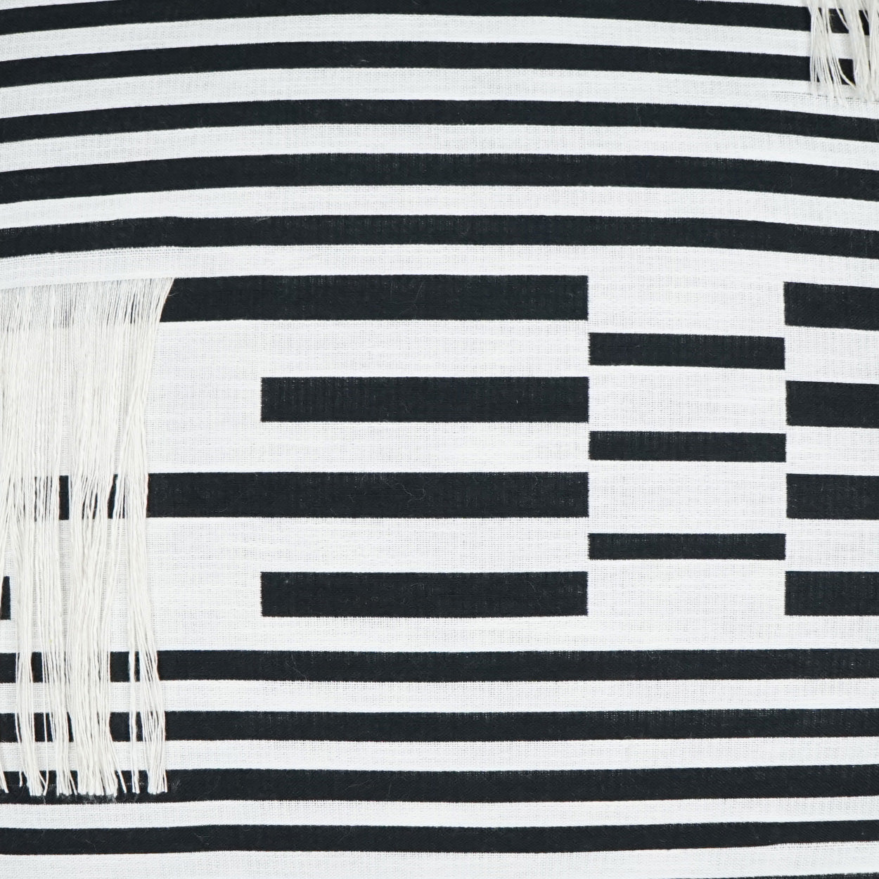 Black and white striped textile with fringe tassels and a geometric rectangular pattern across the fabric.