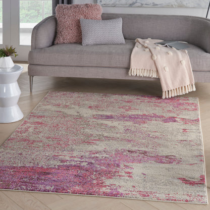 Gray sofa with pink and gray cushions, blush throw blanket, and a beige-pink abstract area rug on light wood floor.