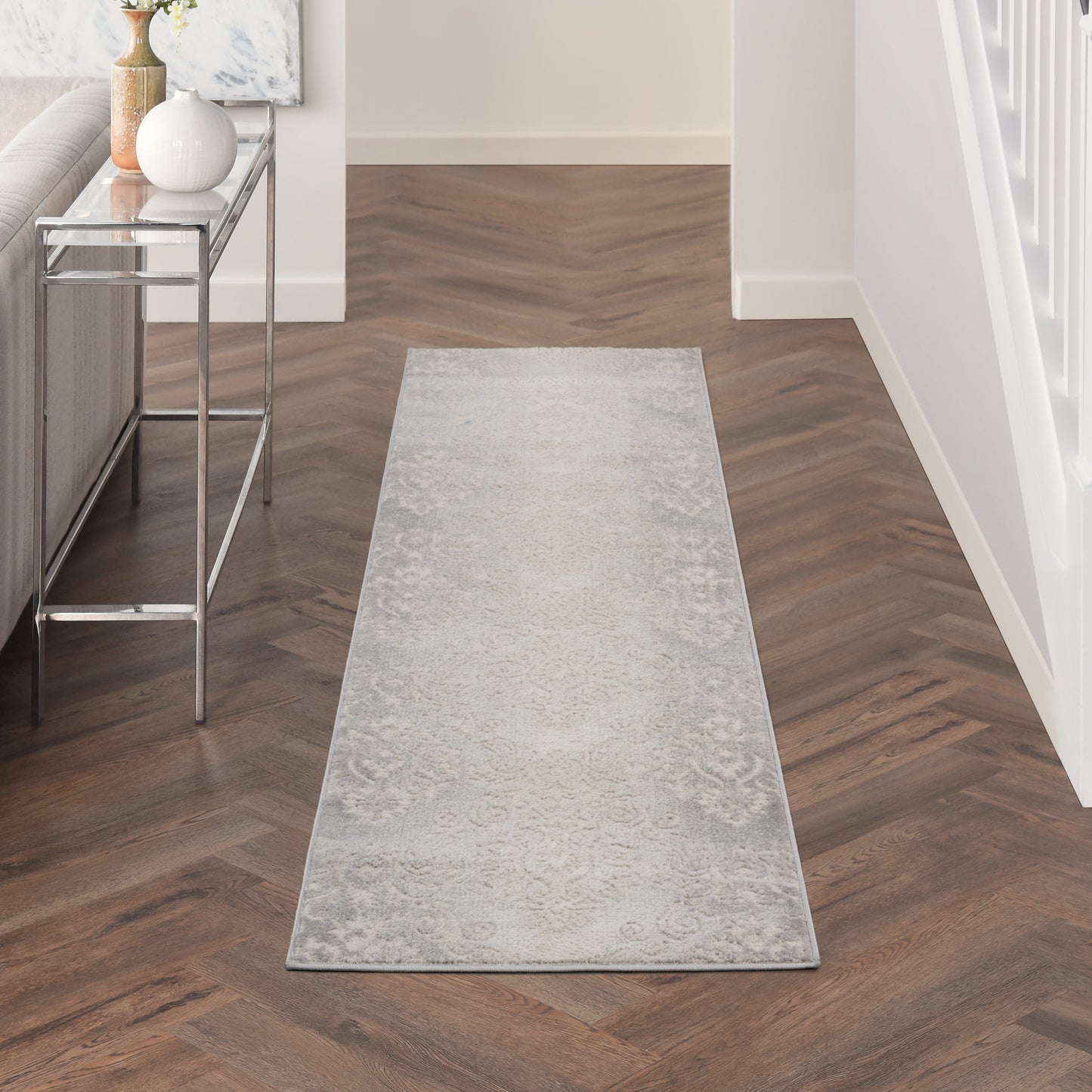 Long light gray hallway runner rug with a subtle faded pattern on dark wood floor beside a metal console table.