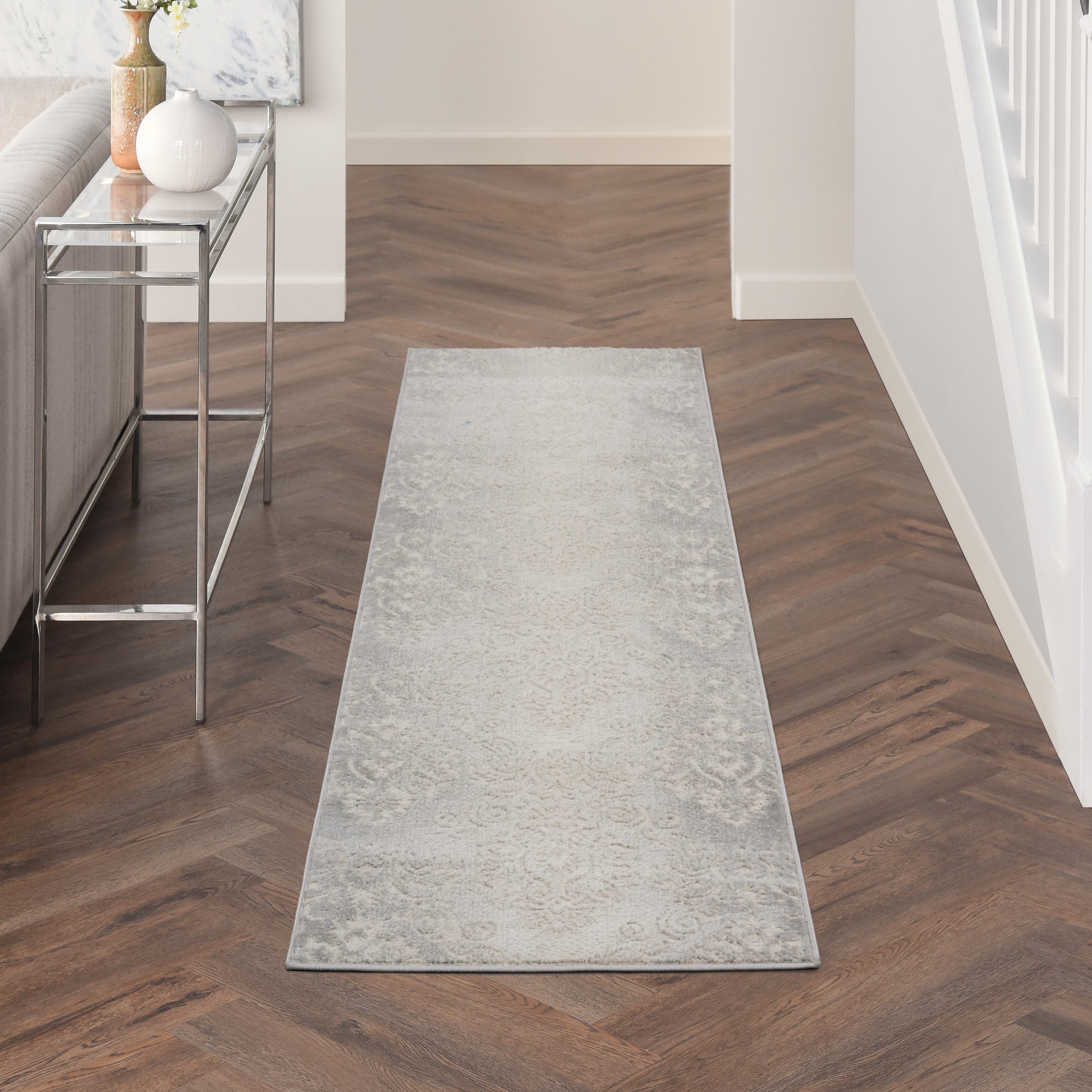 Long light gray hallway runner rug with a subtle faded pattern on dark wood floor beside a metal console table.