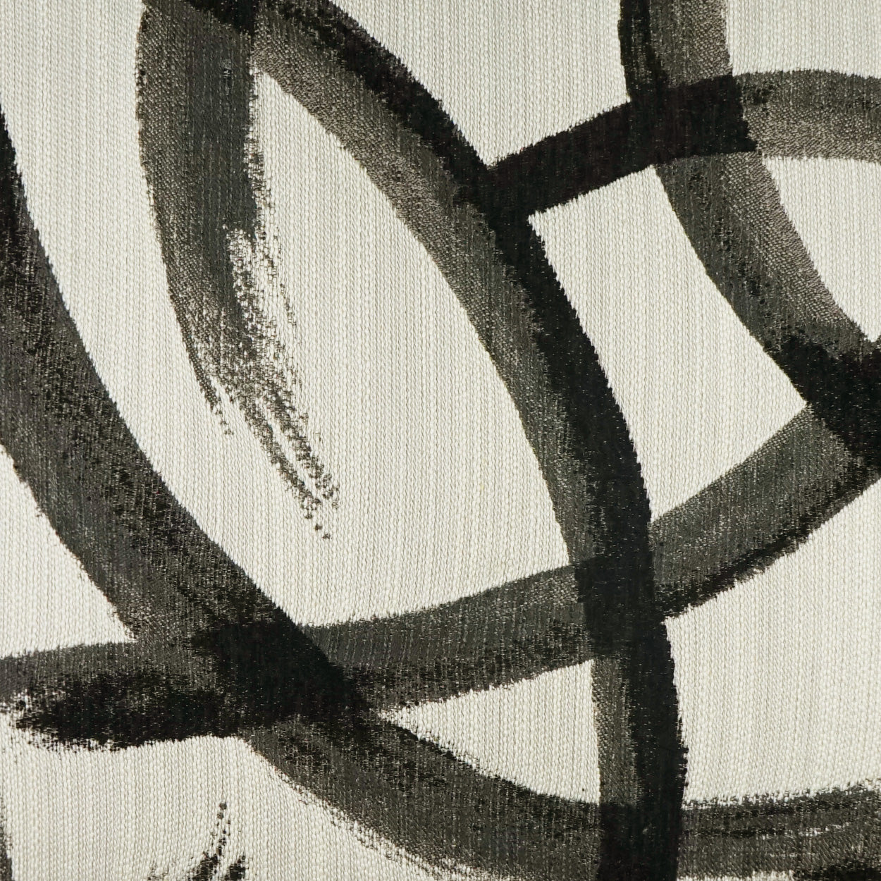 Beige pillow fabric with intersecting black brushstroke lines in an abstract pattern.