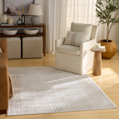 Beige fabric armchair with striped cushion, round wooden side table, candle & books, potted plant in neutral living room.
