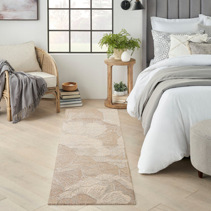 Beige botanical runner rug on light wood floor by bed with white bedding, wicker chair & potted plant on round table.