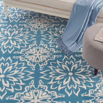 Blue area rug with white damask floral medallion pattern; cozy living room scene with beige sofa and light blue throw.