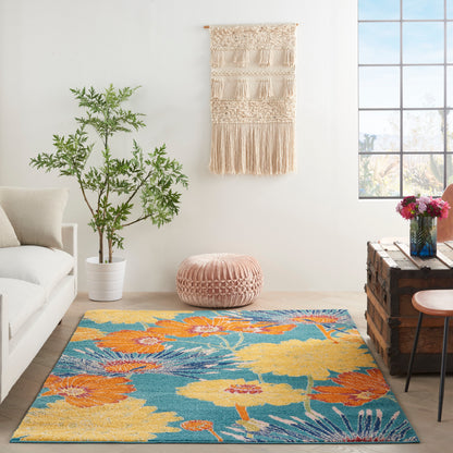 Boho living room with teal floral rug, beige sofa, pink pouf, macramé wall hanging, potted plant, crate coffee table & vase.