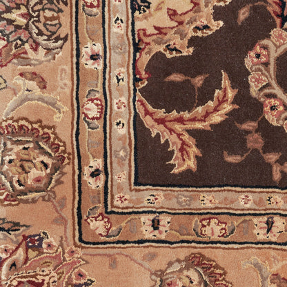 Ornate oriental rug close-up with floral motifs in beige, tan and brown; ivory border with blue and black trim.