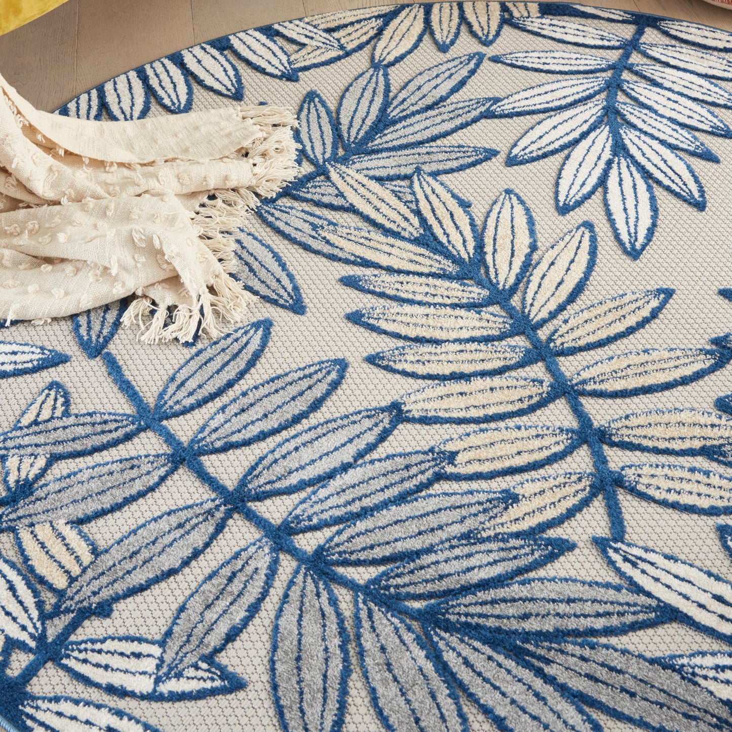 Round woven rug with blue botanical leaf pattern on cream background; boho coastal decor.