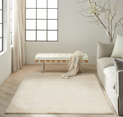 Neutral living room with cream tufted bench, beige rug, gray sofa, large grid windows, light wood floors.