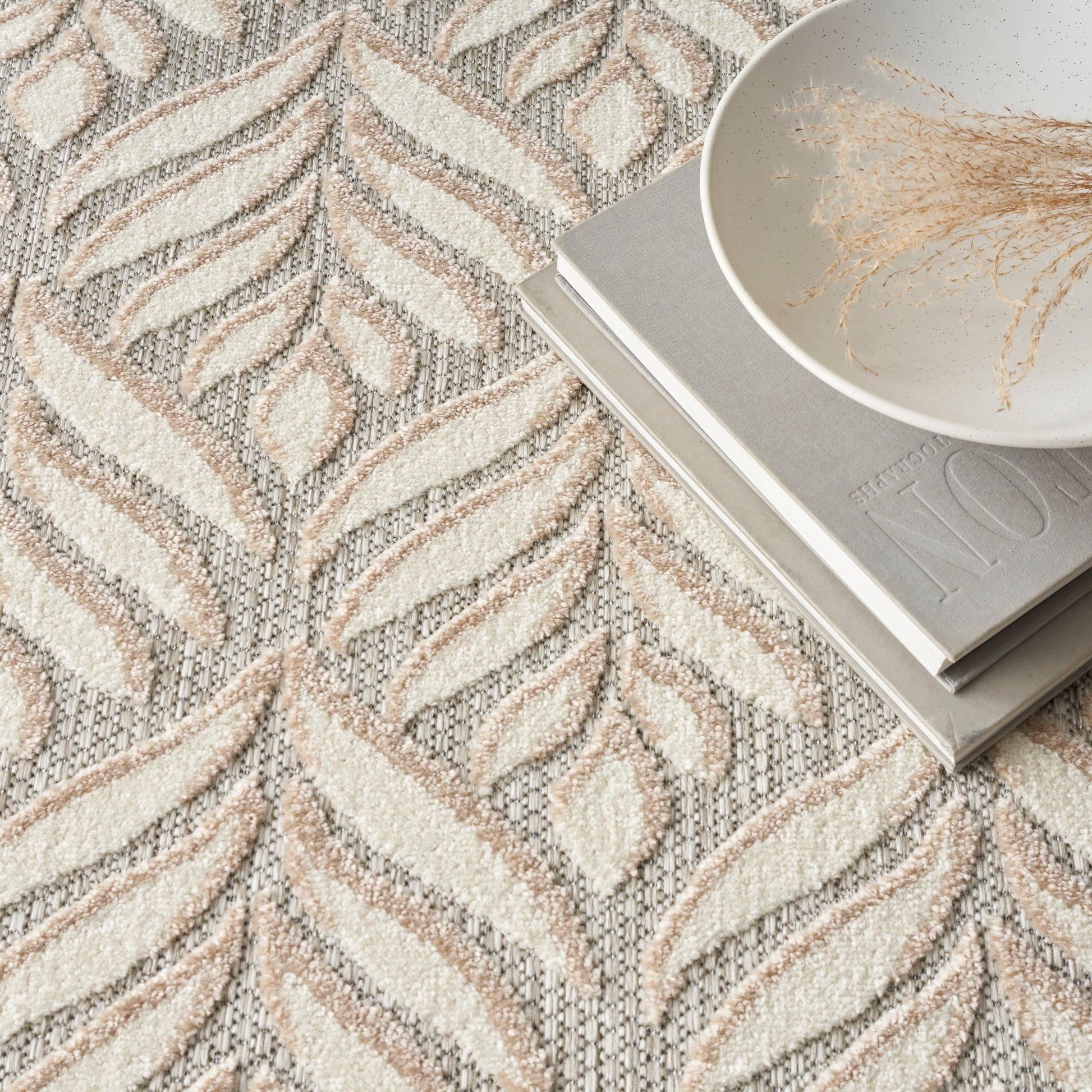 Cream & taupe textured rug with leaf-chevron pattern; white bowl with dried grass on gray magazines.