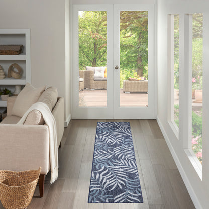 Navy blue rectangular woven runner rug with white palm leaf pattern; indoor living room hallway near glass doors.